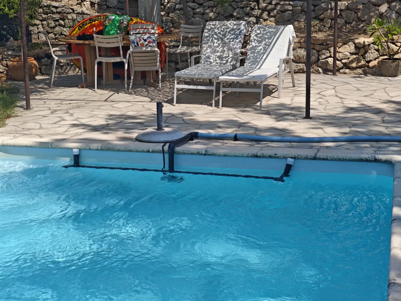 Dérivation de la filtration posée au bord d'une piscine à l'eau bleue, devant une terrasse en pierre