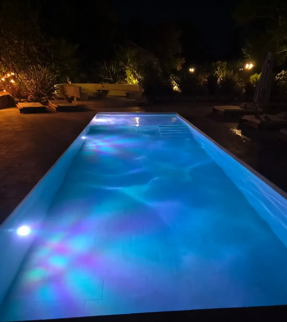 Piscine éclairée de nuit, eau bleue lumineuse et reflets colorés
